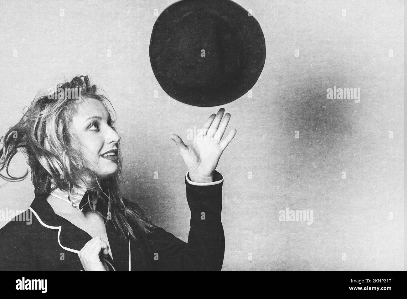 Aged photograph of an elegant blond retro woman throwing and catching hat with hair in motion Stock Photo