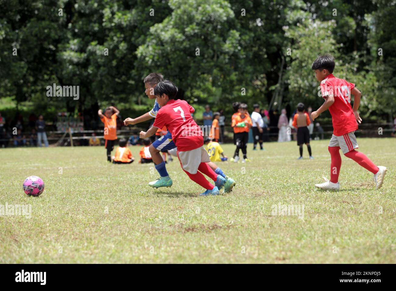 Asian Kids with red and blue uniforms playing football on the soccer