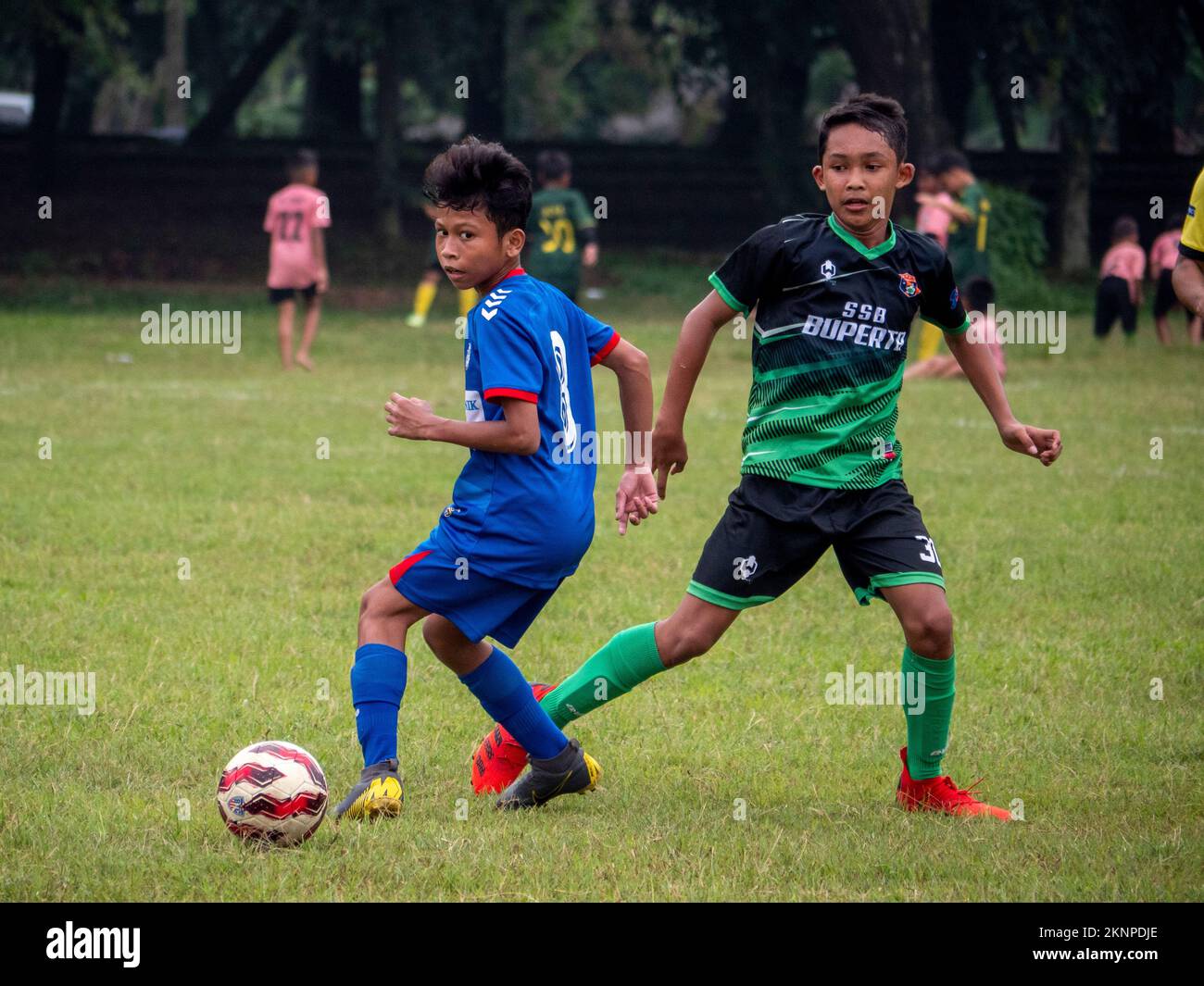 Asian Kids with blue and green uniforms playing football on the soccer