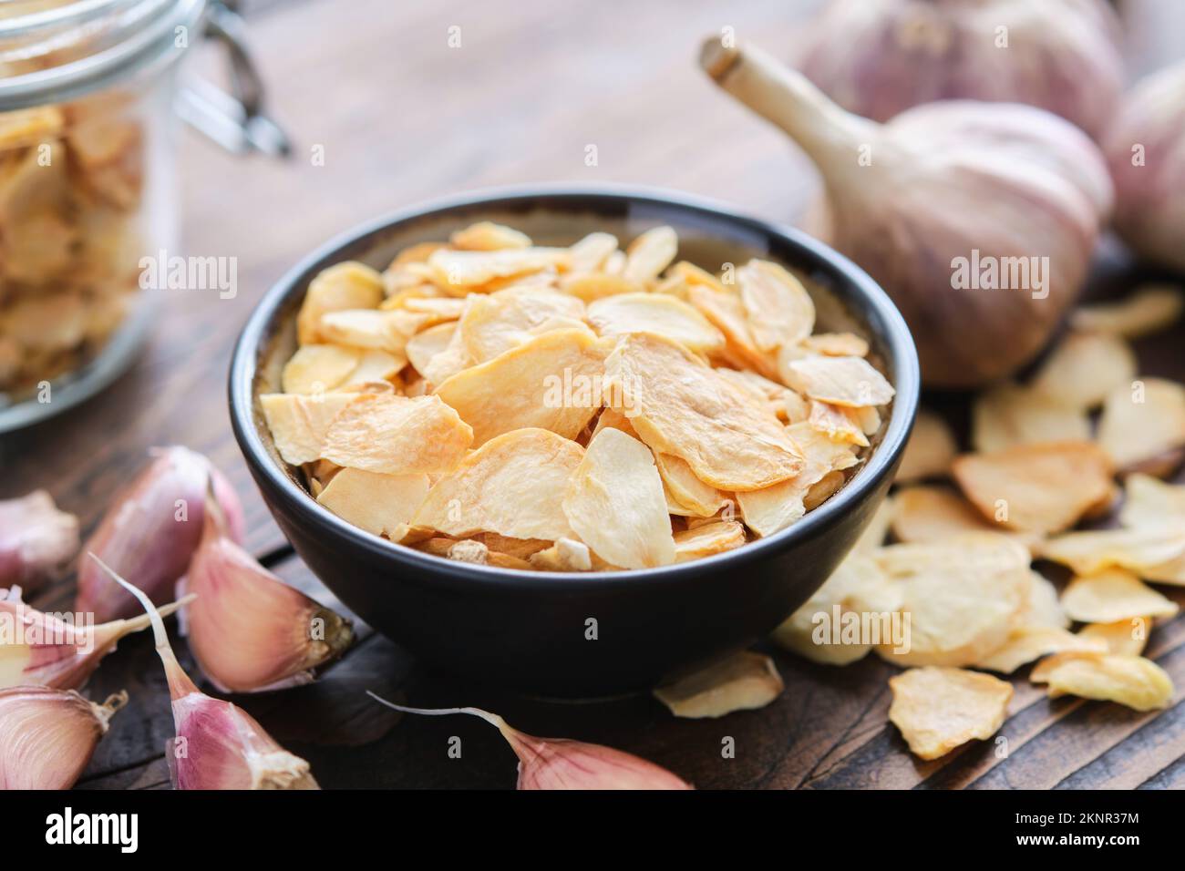 Bowl of dried garlic flakes. Heads of garlic and glass jar of garlic