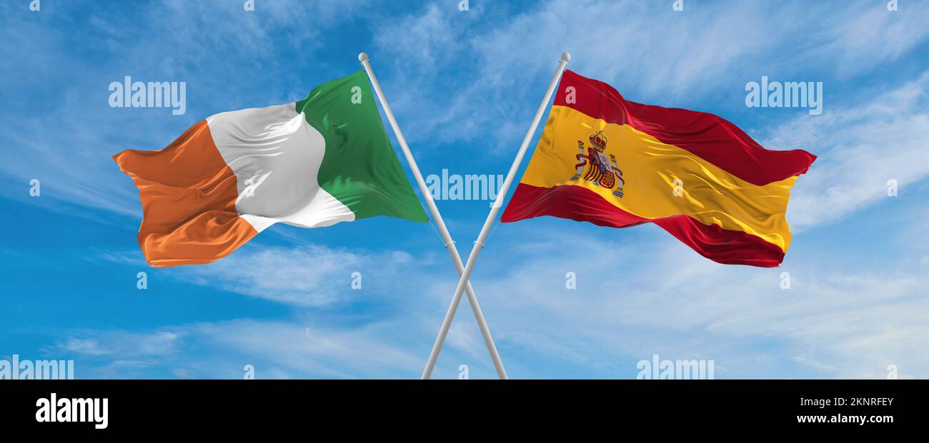 two crossed flags Spain and Ireland waving in wind at cloudy sky ...