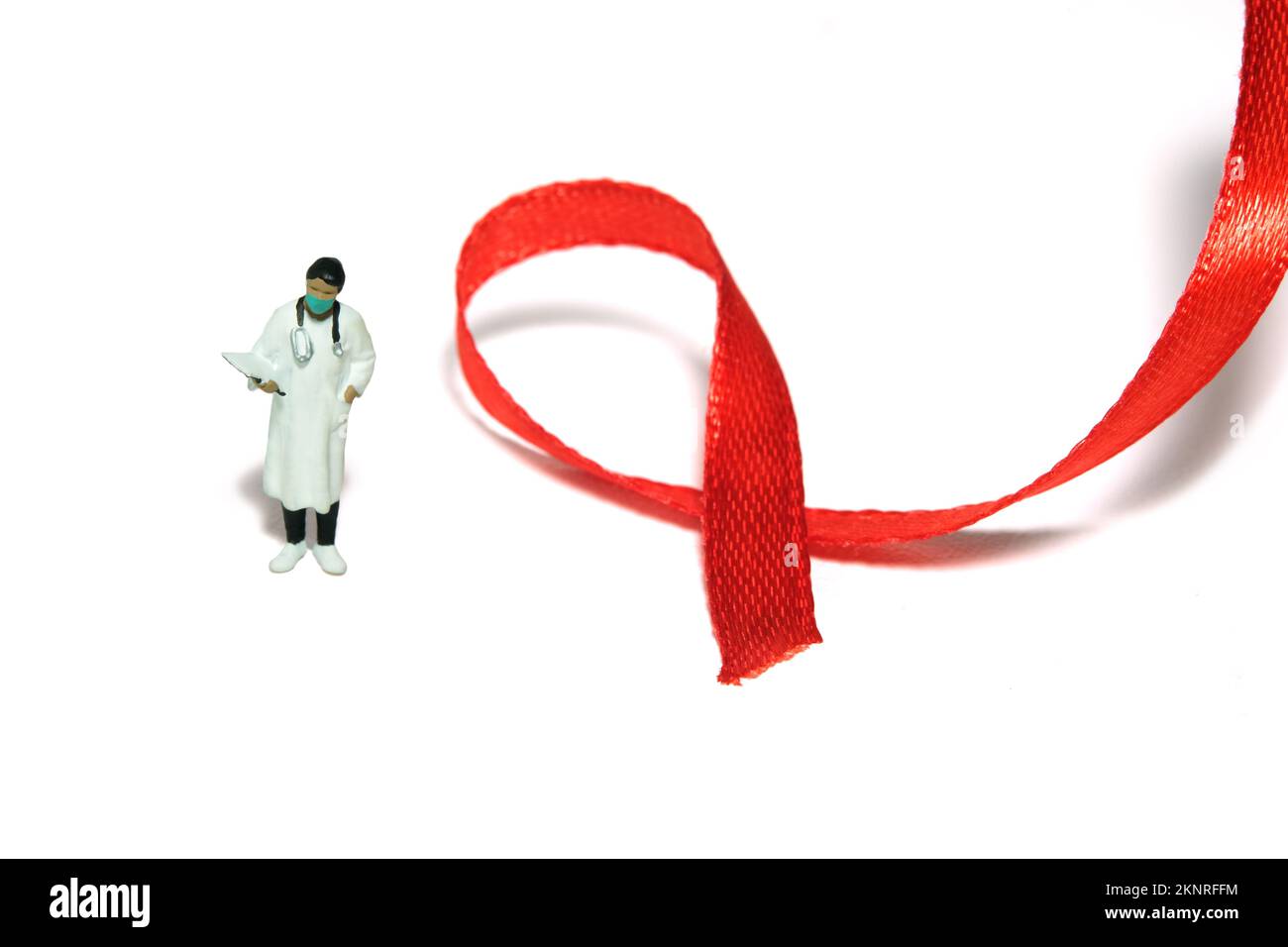 Miniature people figure toys photography. World AIDS Day awareness day concept. Girl woman doctor standing beside red ribbon. Isolated on white backgr Stock Photo