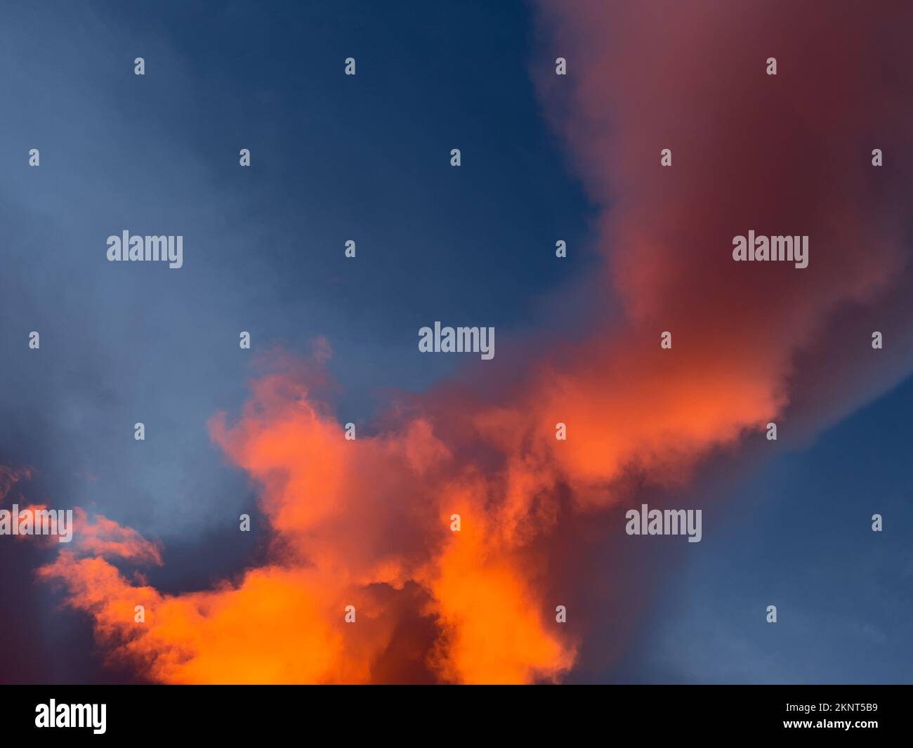Sunrise overhead looks like bright orange fire in the dark blue sky. Clouds are large and swirling. Stock Photo