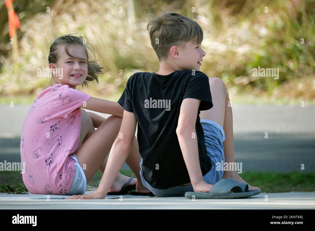 Two happy smiling teenage children, boy and girl sitting outdoors