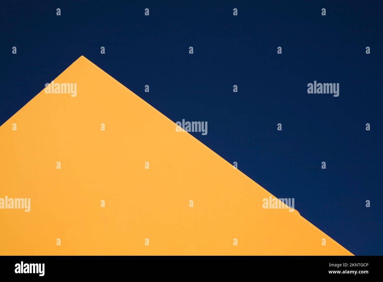 Partial view of a flat yellow metal shaped pyramid against a blue sky background. Stock Photo