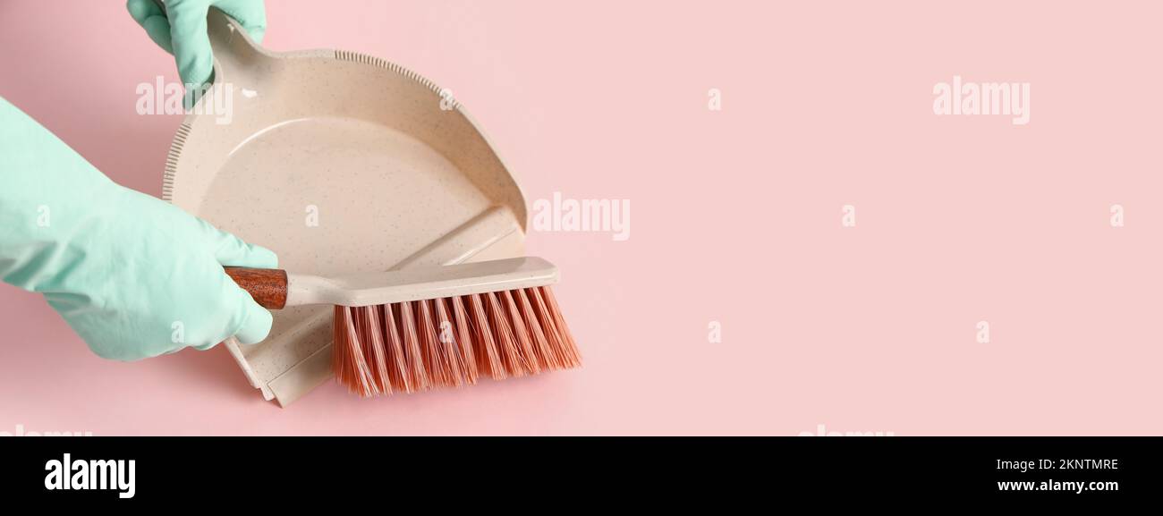 Female hands in rubber gloves with dustpan and brush on pink background