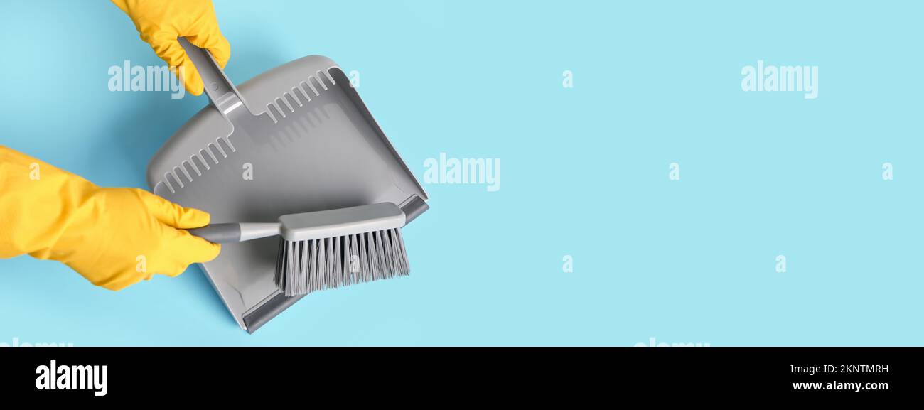 Hands in rubber gloves with dustpan and brush on light blue background