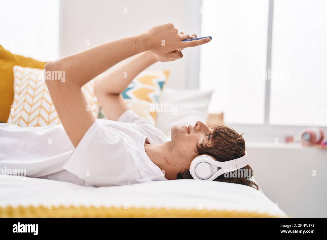 Young blond man listening to music lying on bed at bedroom Stock Photo ...