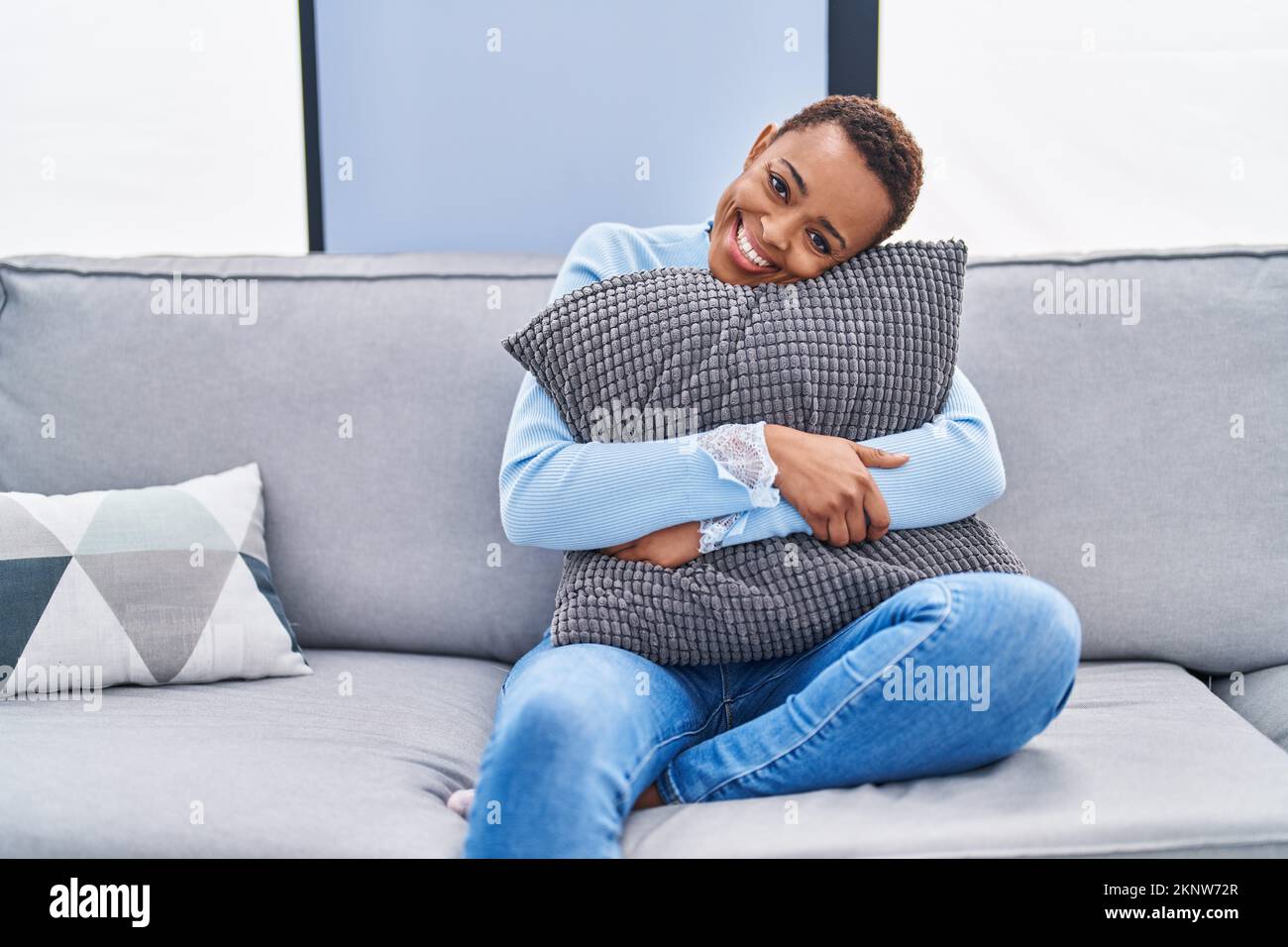 African american woman sitting on the sofa at home hugging pillow ...
