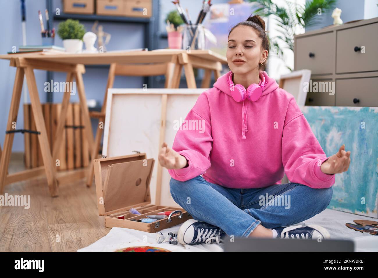 Young woman artist sitting on floor doing yoga exercise at art studio ...