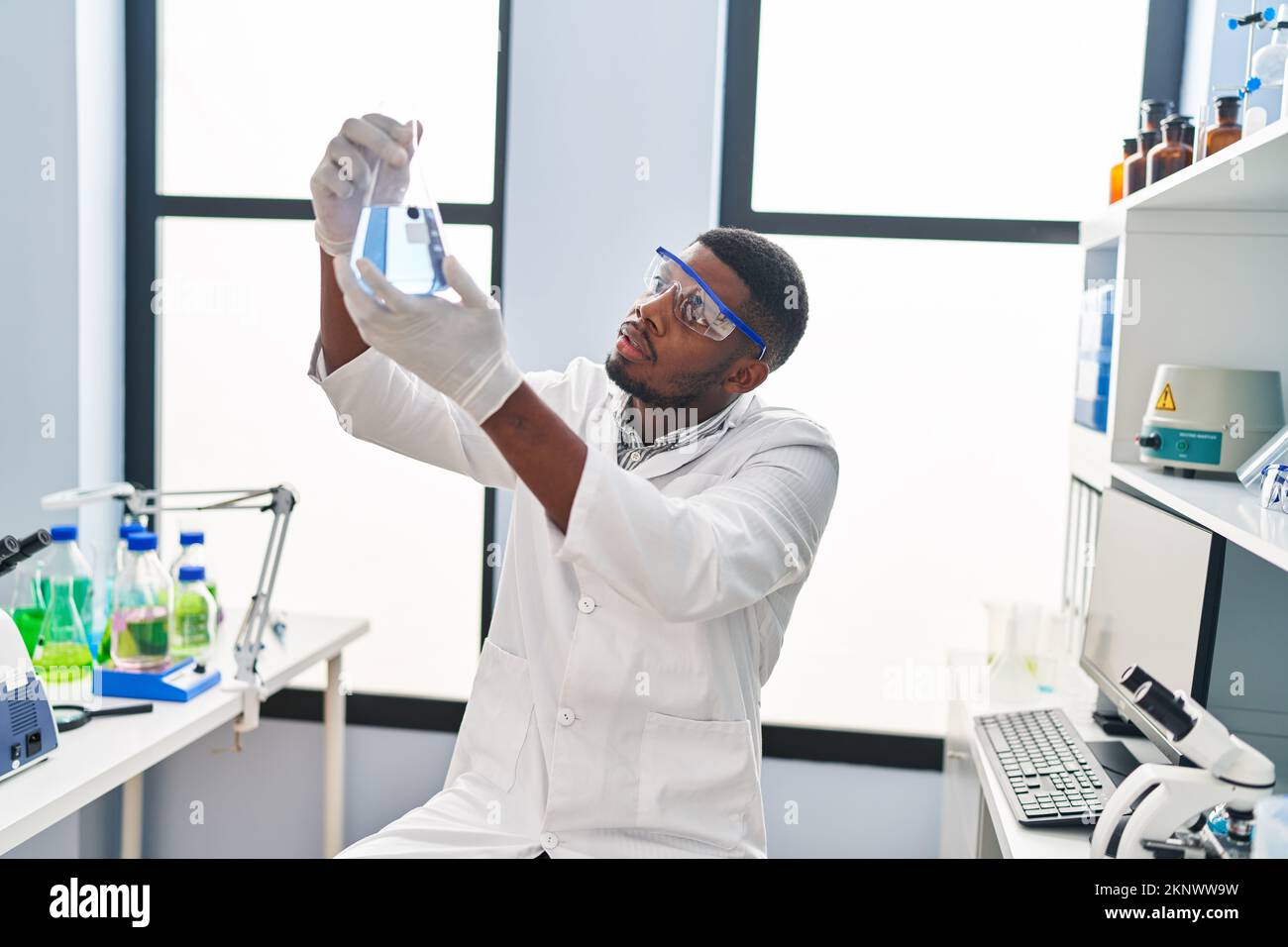 Young african american man wearing scientist uniform holding test tube ...