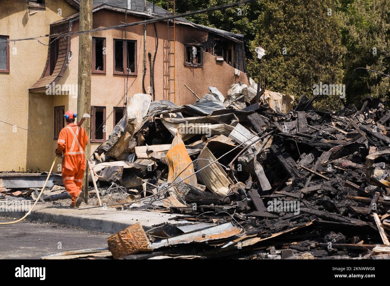 Clean-up worker next to fire damaged cottage style home with remnants of a burnt down commercial building. Stock Photo