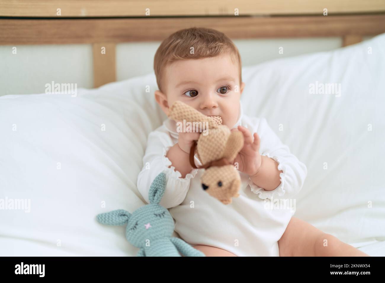 Adorable toddler sitting on bed bitting doll at bedroom Stock Photo - Alamy