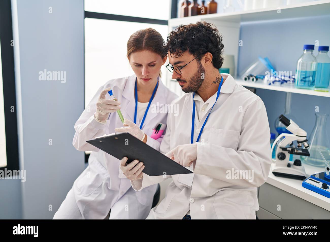 Man and woman scientist partners looking test tube holding clipboard at ...