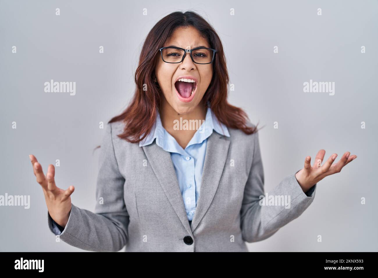 Hispanic young business woman wearing glasses crazy and mad shouting