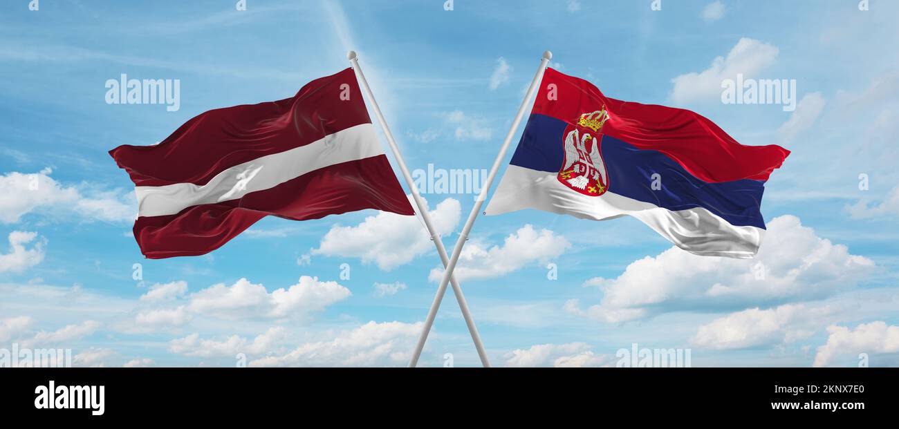 two crossed flags Serbia and Latvia waving in wind at cloudy sky ...