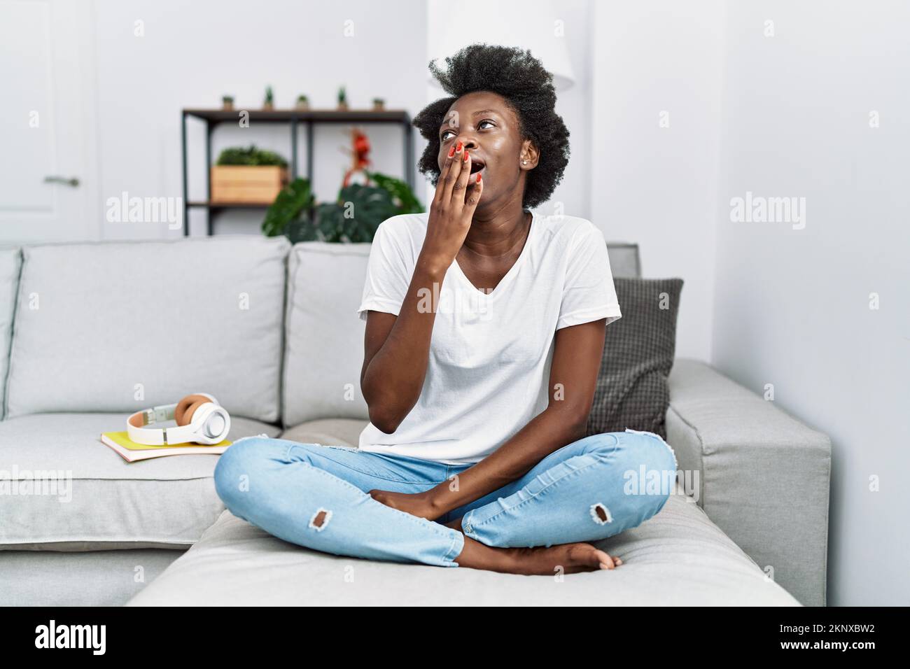 African young woman sitting on the sofa at home bored yawning tired ...