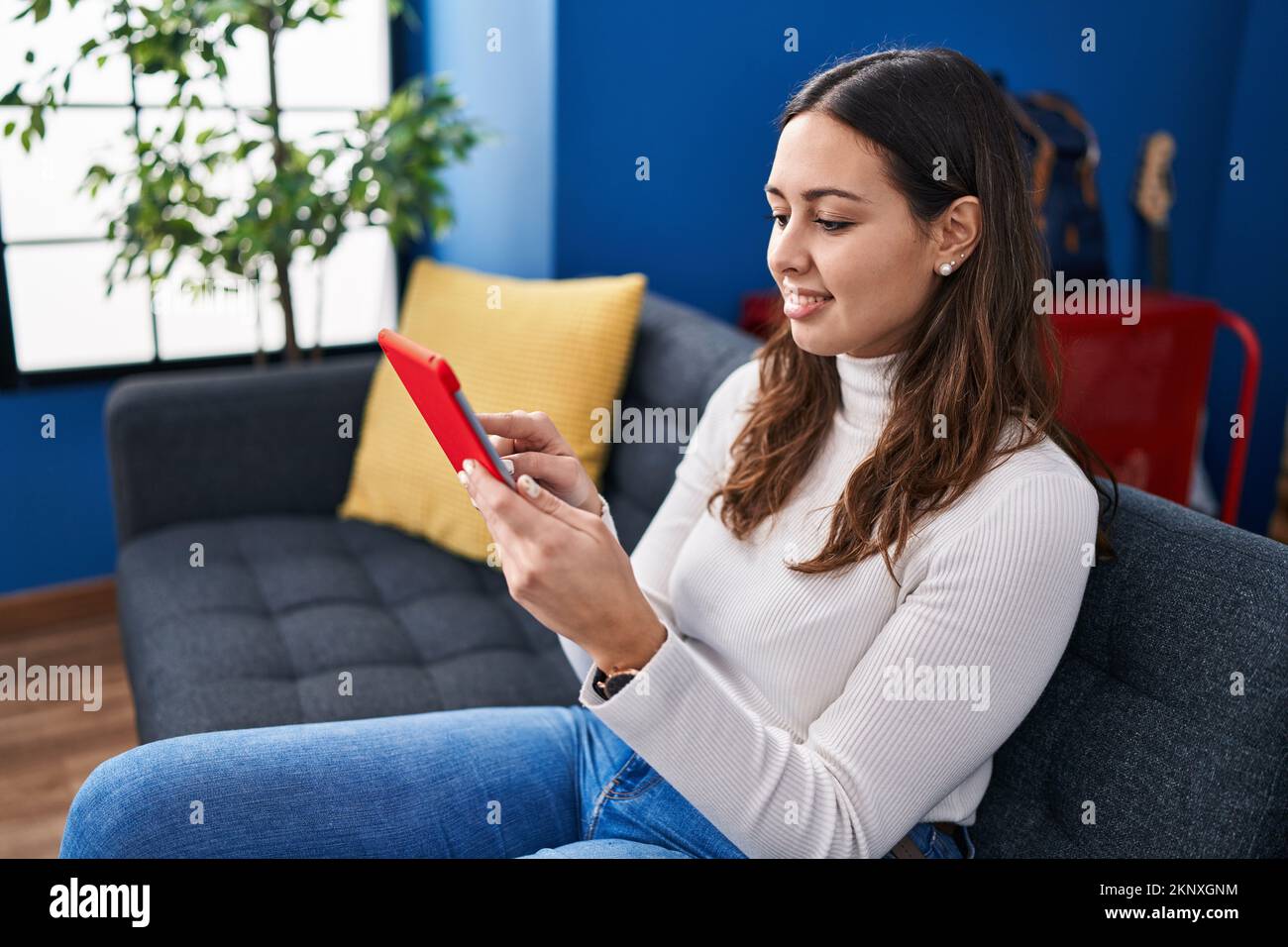 Young beautiful hispanic woman using touchpad sitting on sofa at home ...