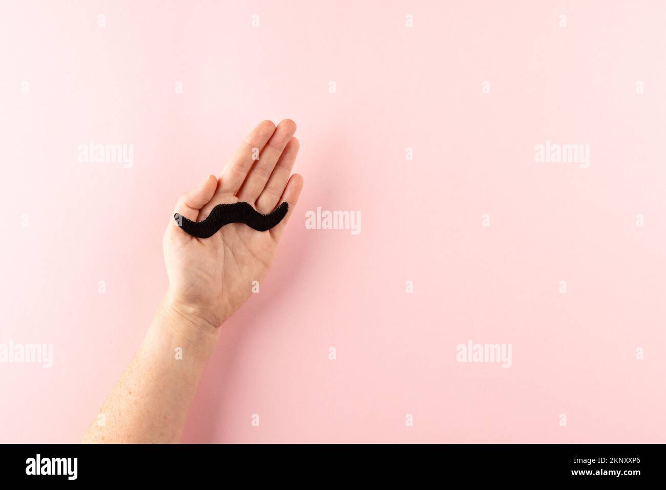 Hand holding black false moustache on pink background, with copy space Stock Photo