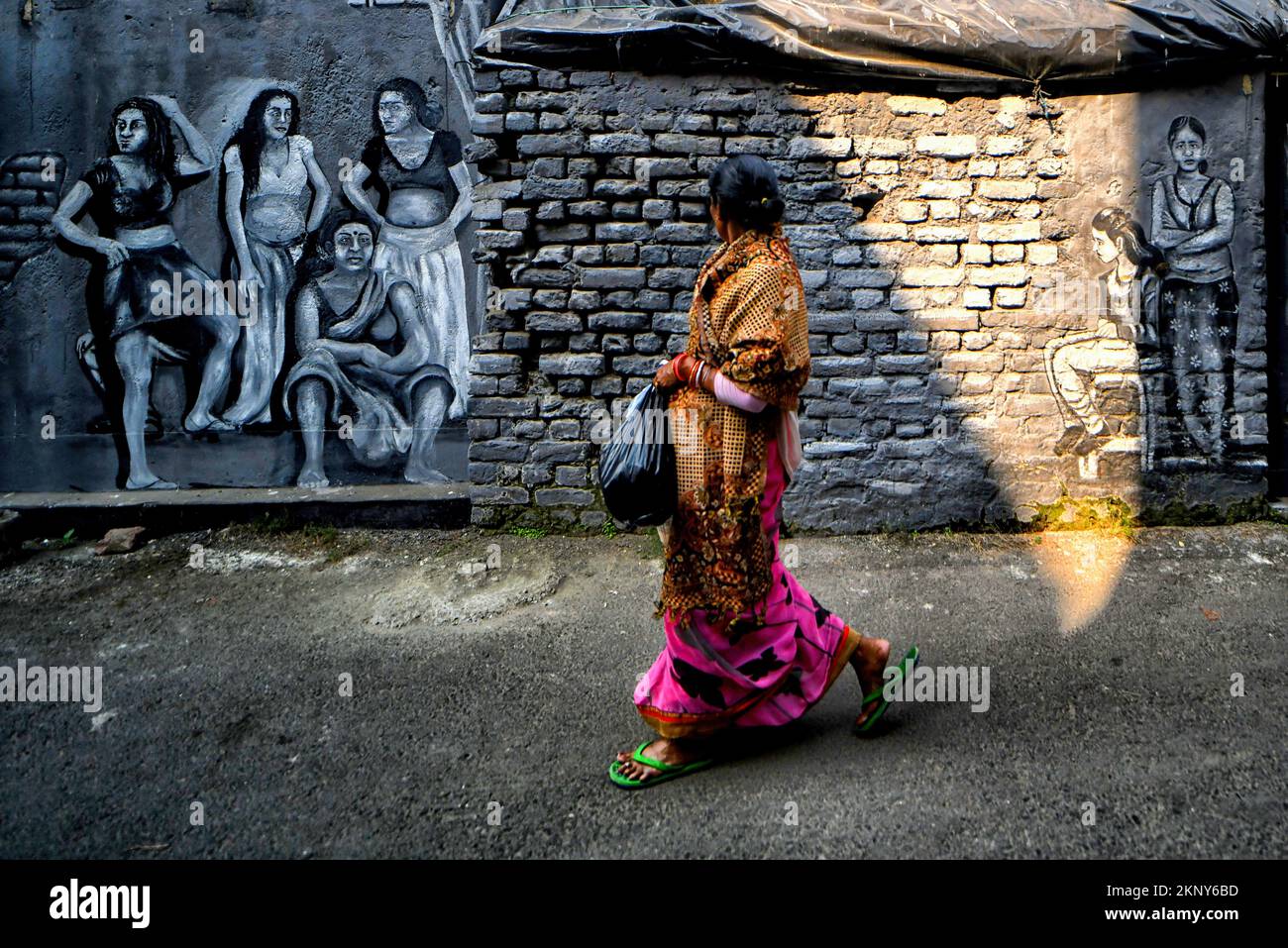 Kolkata, India. 26th Nov, 2022. A woman walks past graffiti mural artwork on a wall. Kolkata Streets and different slums seen getting painted with colorful graffiti as an initiative by a Football Club (Milan Sangha) in Kolkata. Artists from different Art colleges have participated to make the city more beautiful. Credit: SOPA Images Limited/Alamy Live News Stock Photo