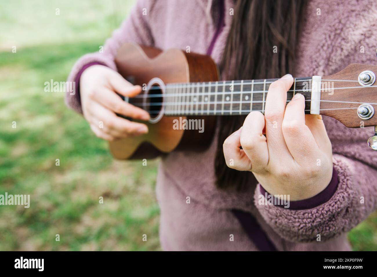 Unrecognizable female person playing ukelele standing on the grass. Stock Photo
