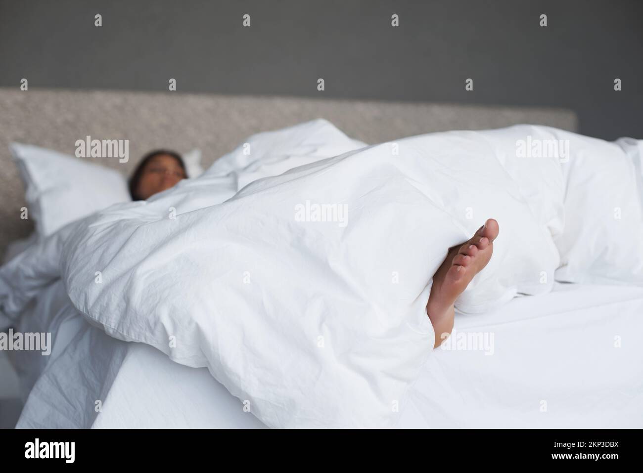 Loving this Saturday morning lie in. a young womans feet sticking out of the duvet as she sleeps. Stock Photo