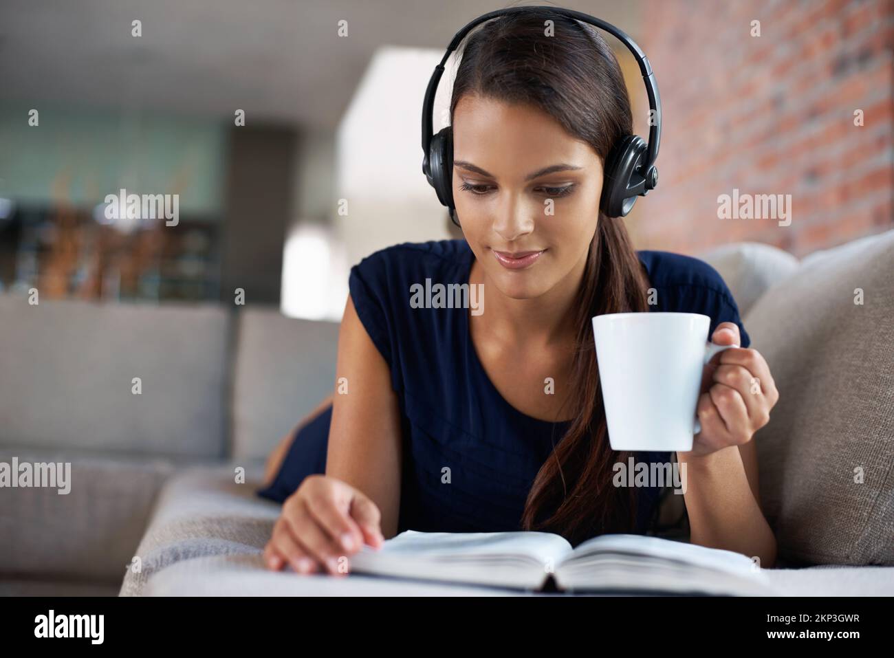 Catching up with hobbies. a beautiful young woman relaxing on her couch with music and a good book. Stock Photo