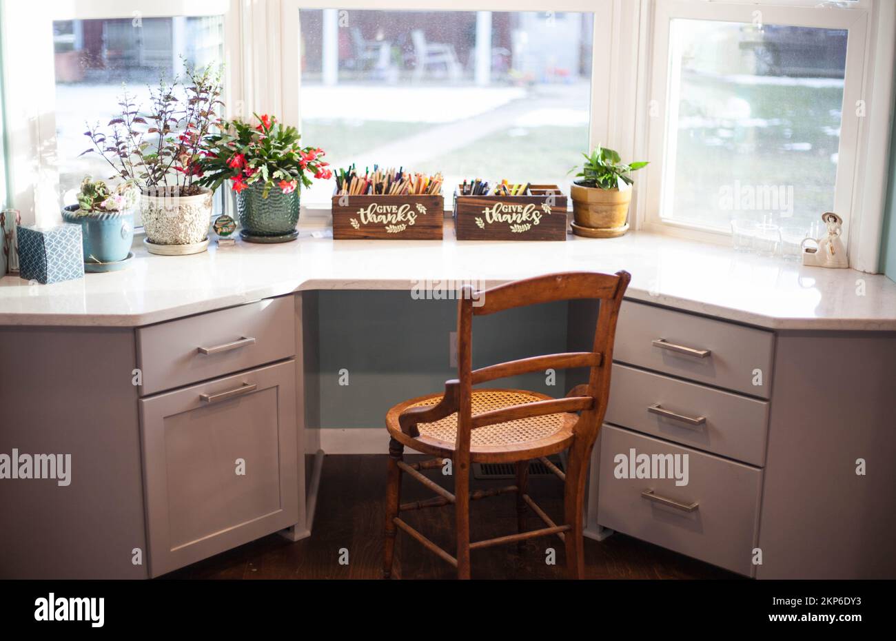 A clean desk in front of a window with house plants and arts and crafts tools with a wooden chair behind Stock Photo