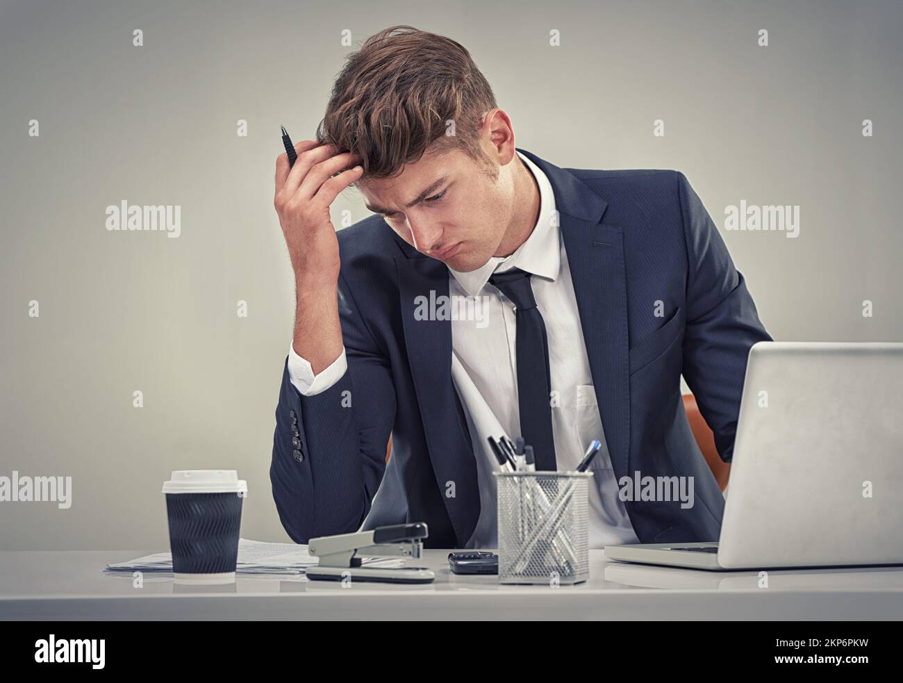 Feeling the strains of a huge corporate job. a young businessman looking deep in thought while sitting at his desk. Stock Photo