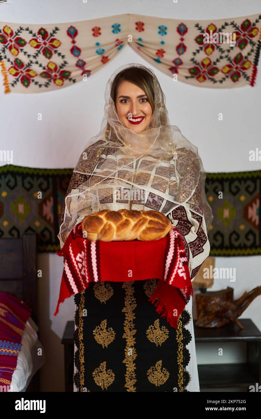Young Romanian woman dressed up in traditional popular costume, in a traditional rural home Stock Photo