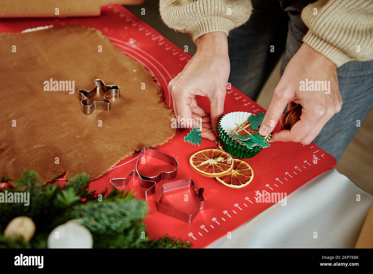 Woman preparing gingerbread cookies at kitchen with Christmas decorations. Female hands cutting ginger dough with cutter to making cookies for winter Stock Photo