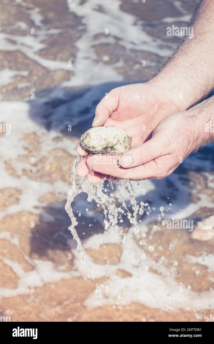 Photograph of the hands of a man washing a Pumicestone in the waters of