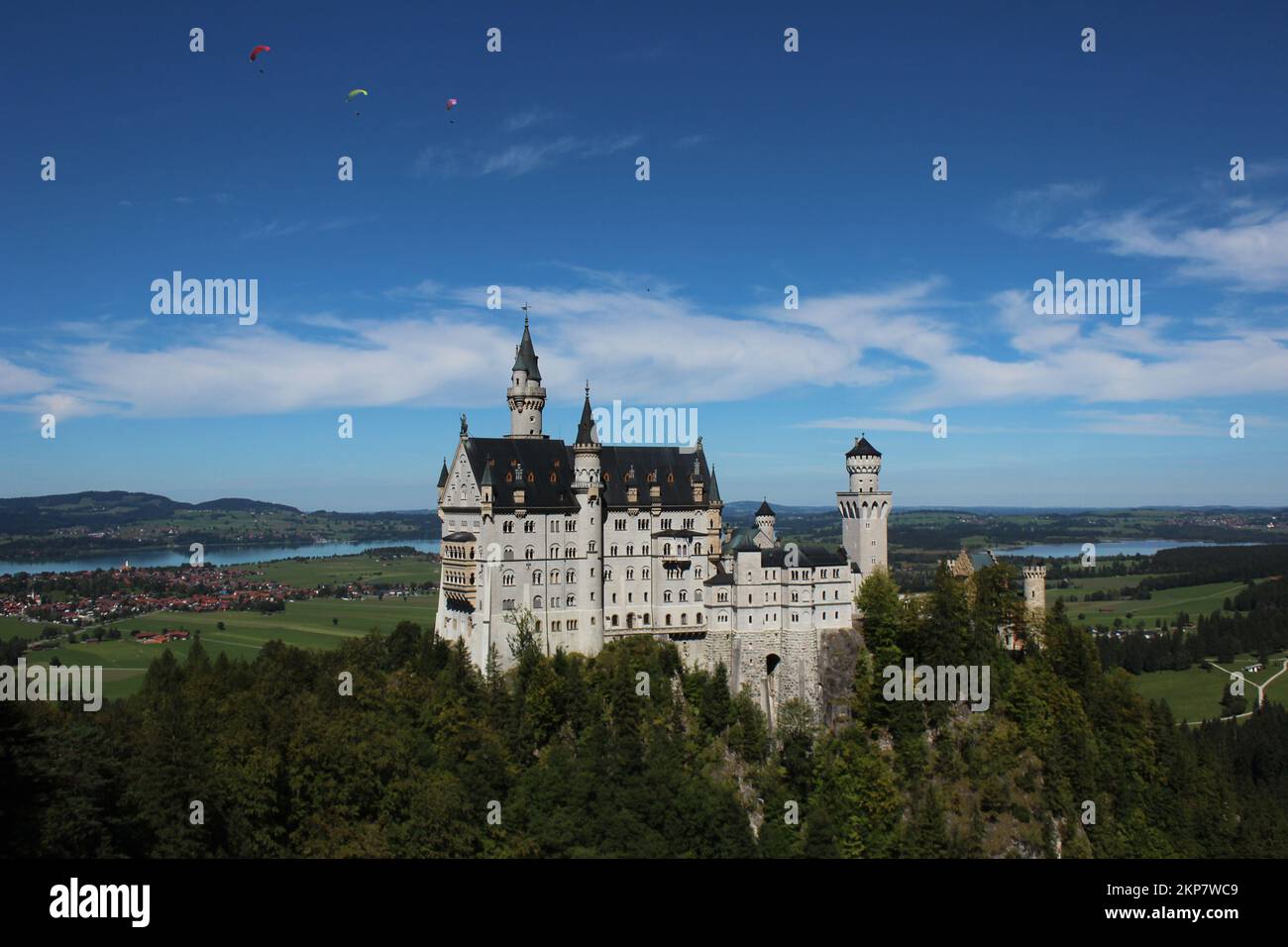 The Neuschwanstein Castle surrounded by trees with a cloudy blue sky background Stock Photo