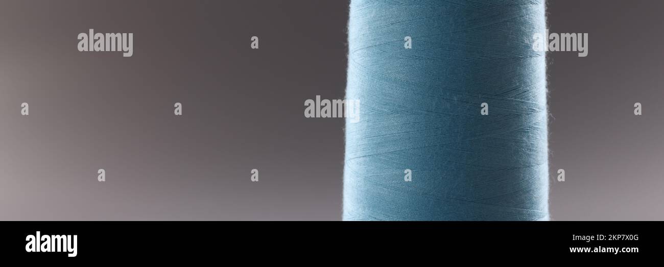 Blue colour thread spool on grey background, thread for dressmaking industry, yarn for sewing Stock Photo