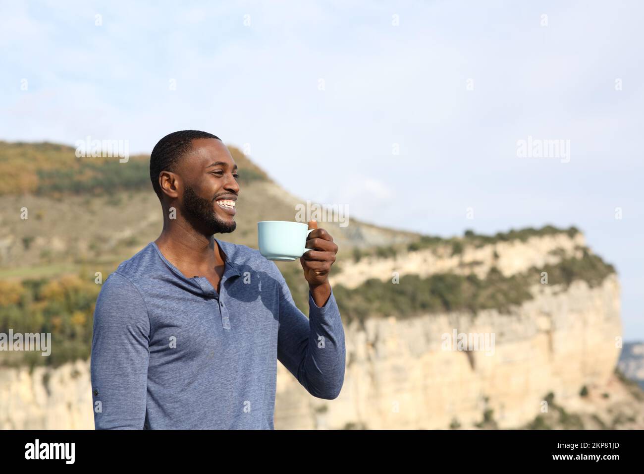 Happy black man drinking coffee contemplating views in the mountain Stock Photo