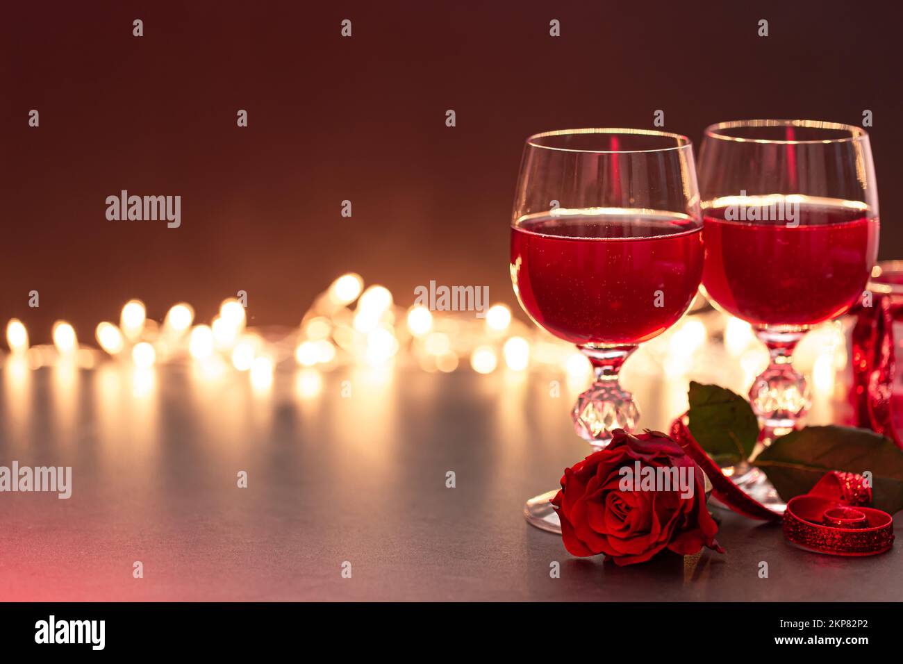 Two glasses of wine and a red rose on a blurred background with bokeh ...