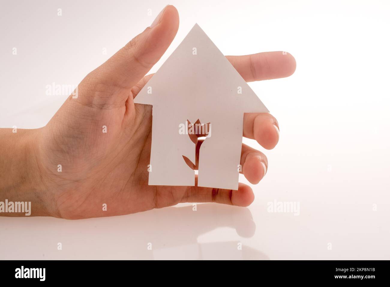 Hand holding a paper house with a flower shape carved in it on a white ...