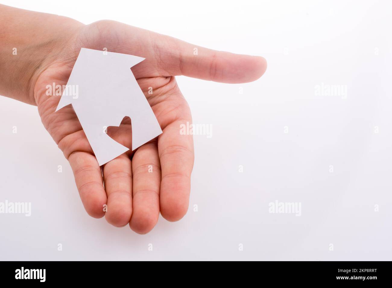 Hand holding a paper house with a heart carved in it on a white ...