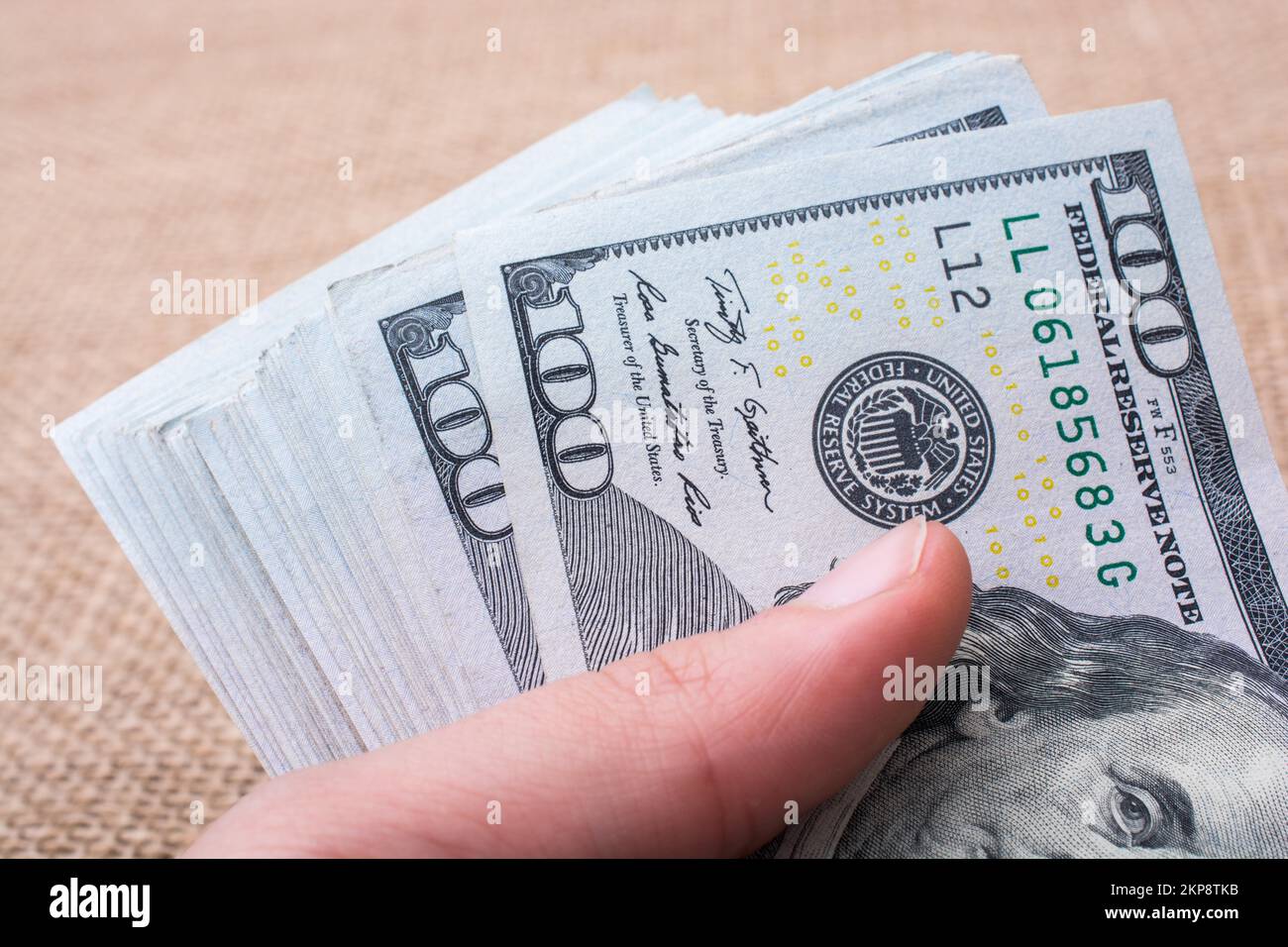 Hand holding banknote bundle of US dollar on a linen canvas background ...