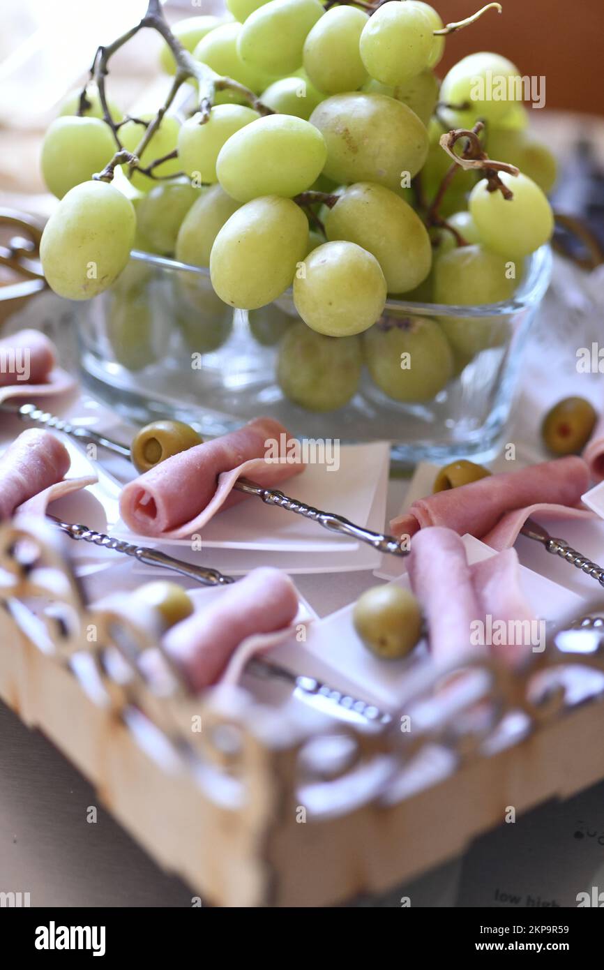 A vertical closeup of a table decoration with snacks like green grapes and ham with green olives Stock Photo