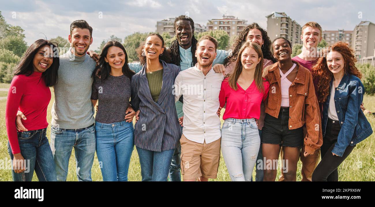 Large group of multiethnic friends posing hugging outdoors smiling and looking at camera - diversity, friendship, oneness, union and people lifestyle Stock Photo