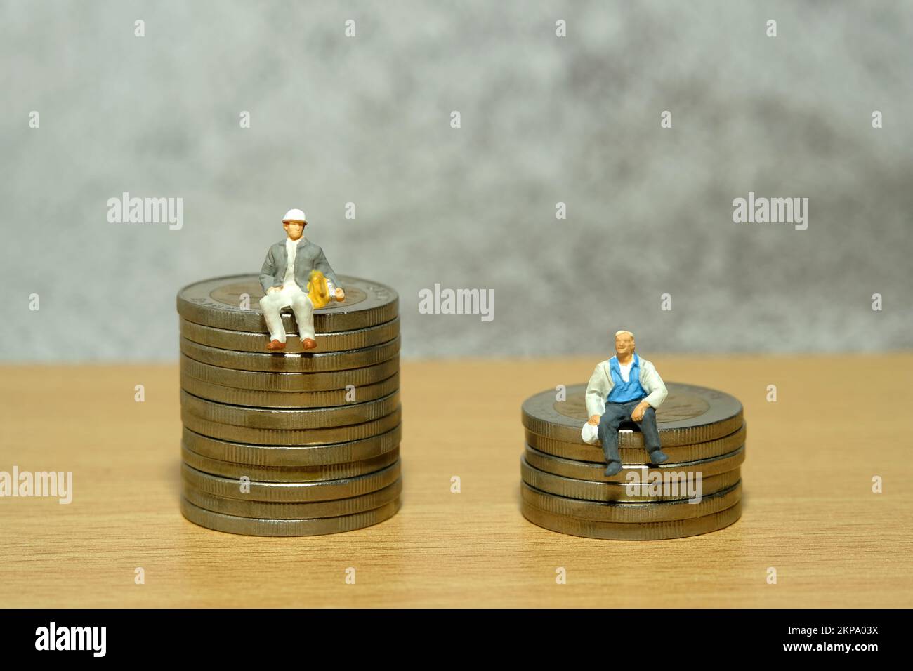 Miniature people toy figure photography. Income and wealth gap, inequality. Two people with different jobs sitting above coin pile. Image photo Stock Photo