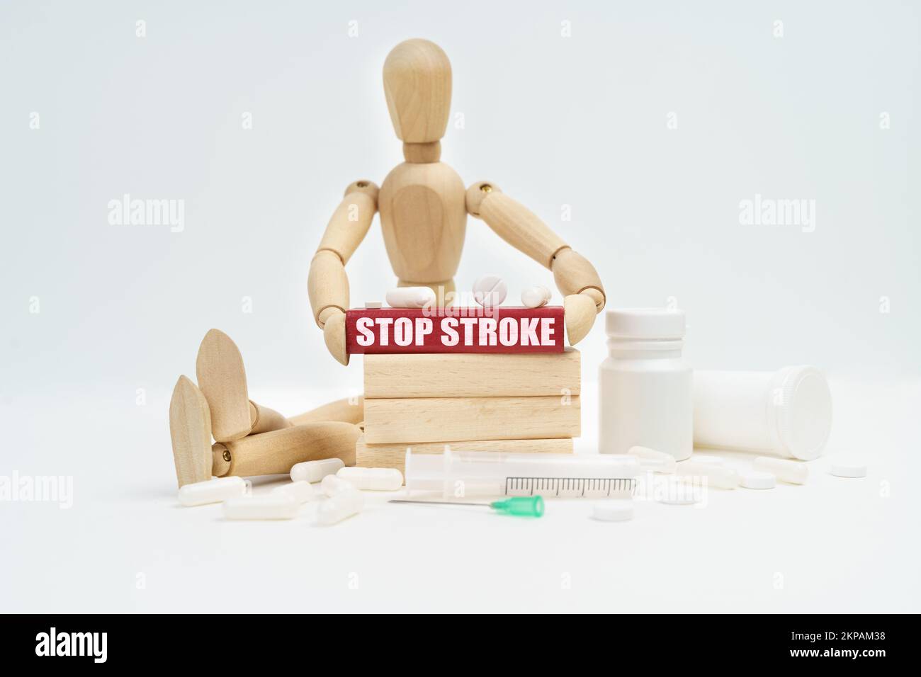 Medicine and healthcare concept. A figurine of a man sitting among pills lifts a red wooden block with an inscription STOP STROKE from a wall of block Stock Photo