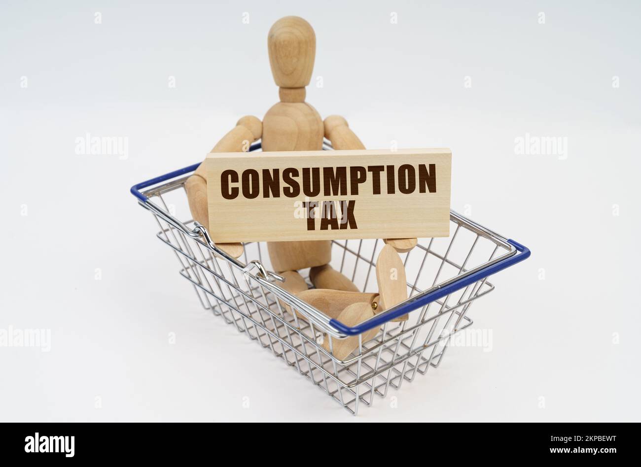 Business and finance concept. A wooden man sits in a shopping basket, holding a sign in his hands - Consumption Tax Stock Photo