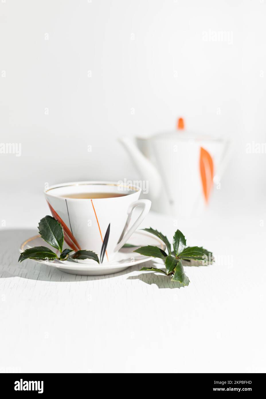 A branch and leaves of Yaupon holly lie near a porcelain cup and teapot