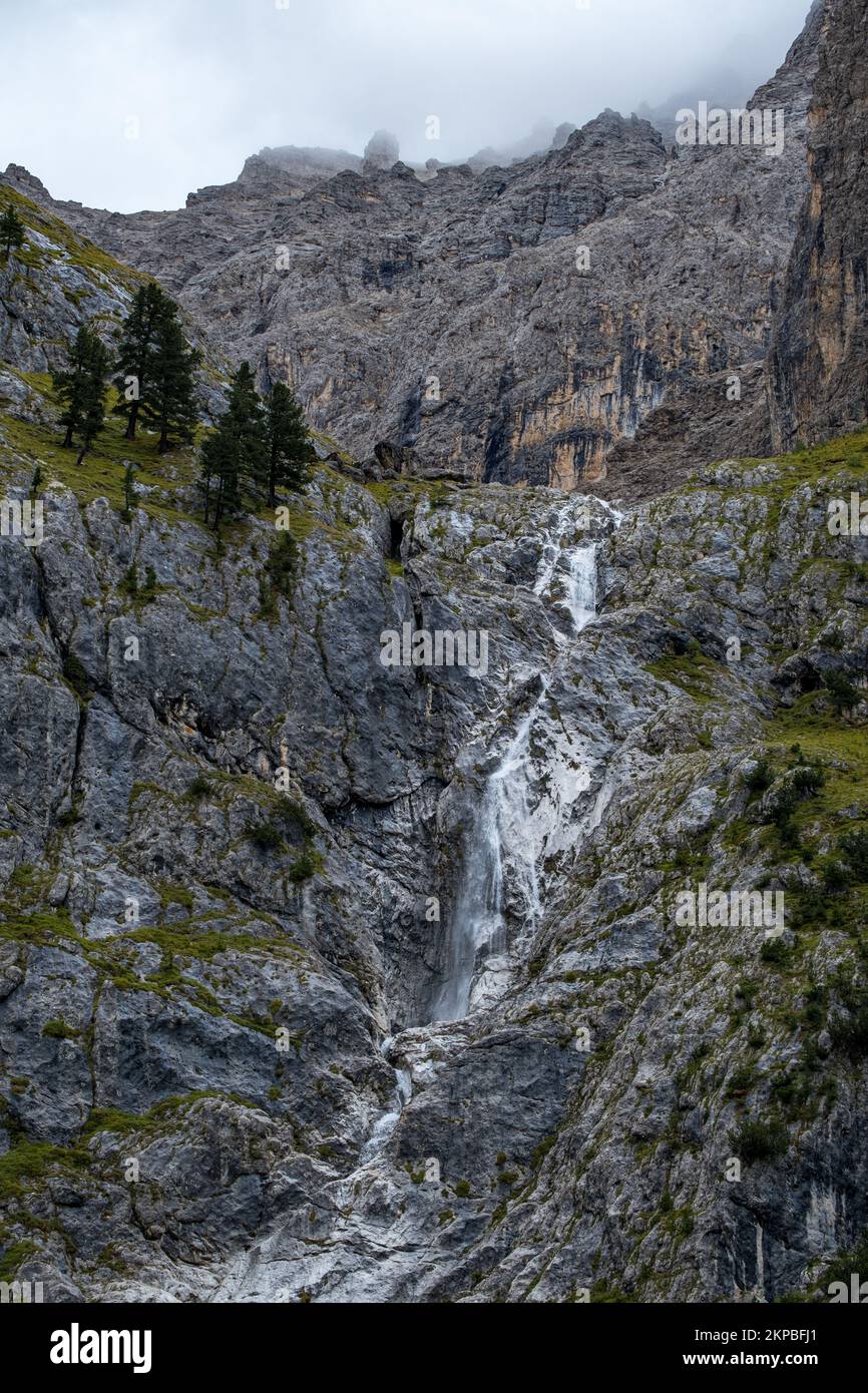 A landscape view with a waterfall in the mountain and green trees in the Sella Pass, South Tyrol Stock Photo