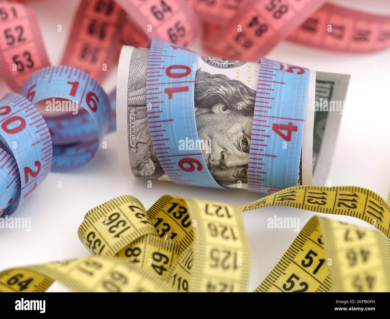A one hundred dollar bill with a tape measure wrapped around it near other tape measures. Close up. Stock Photo