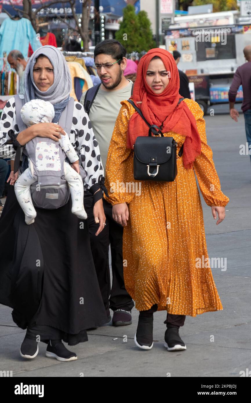 Women in hijabs, one holding a child walk through Diversity Plaza on a mild autumn say. InJackson Heights, Queens New York City. Stock Photo