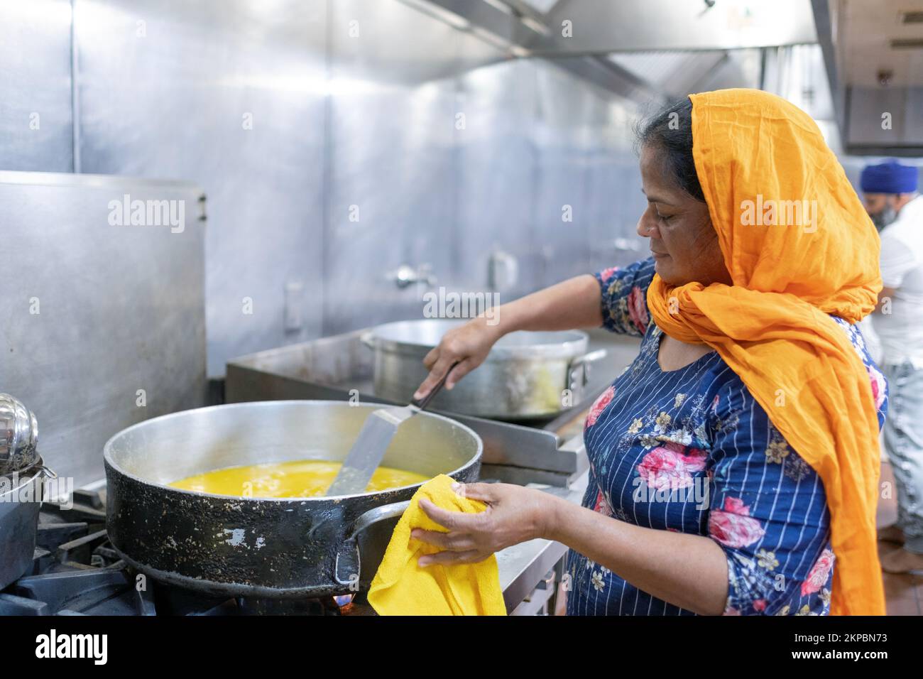 A cook in a Sikh kitchen cooking in an extremely large pot.