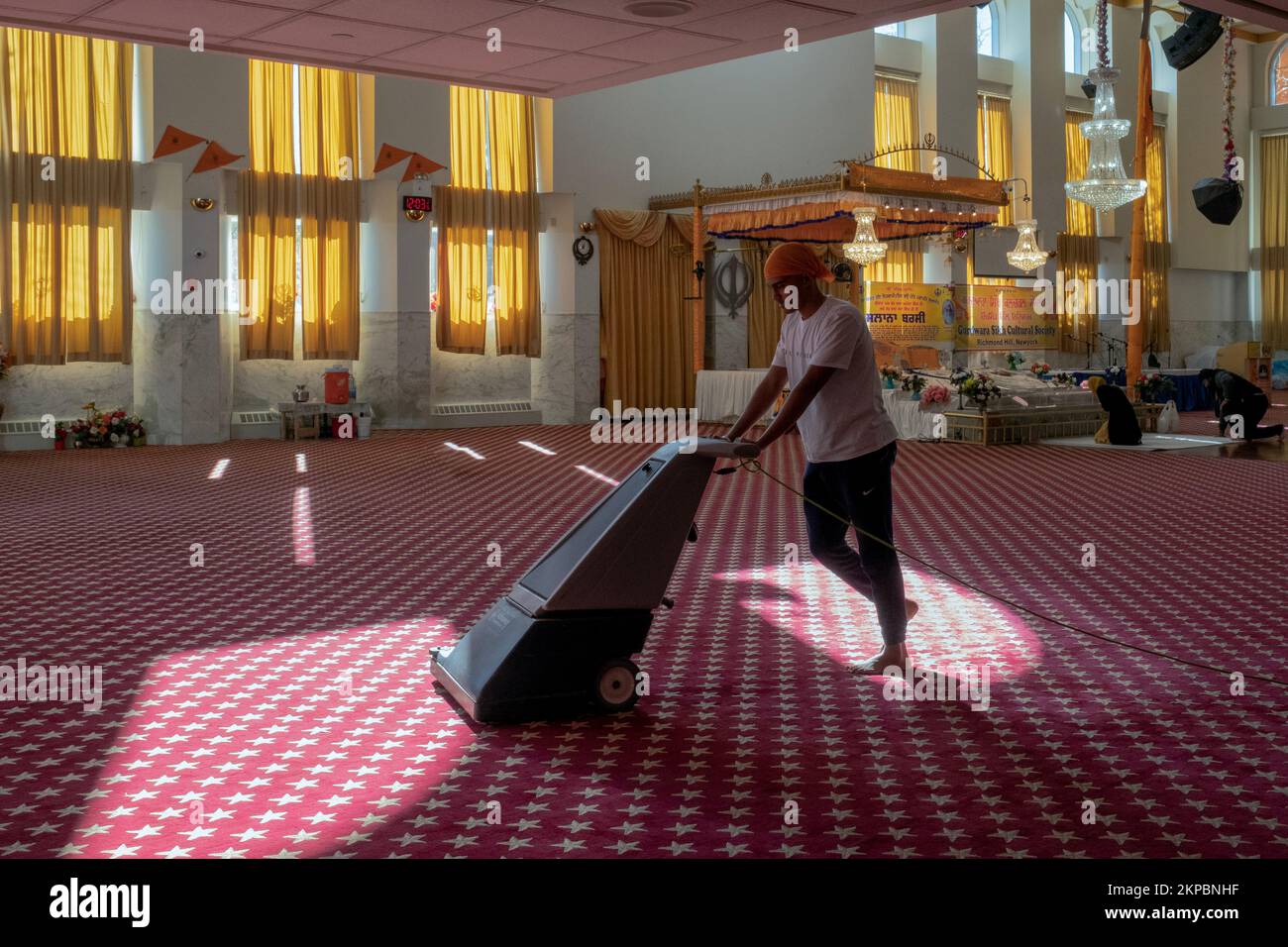 A teenage volunteer vacuums the carpet at a Sikh temple in Queens, New York City. Stock Photo